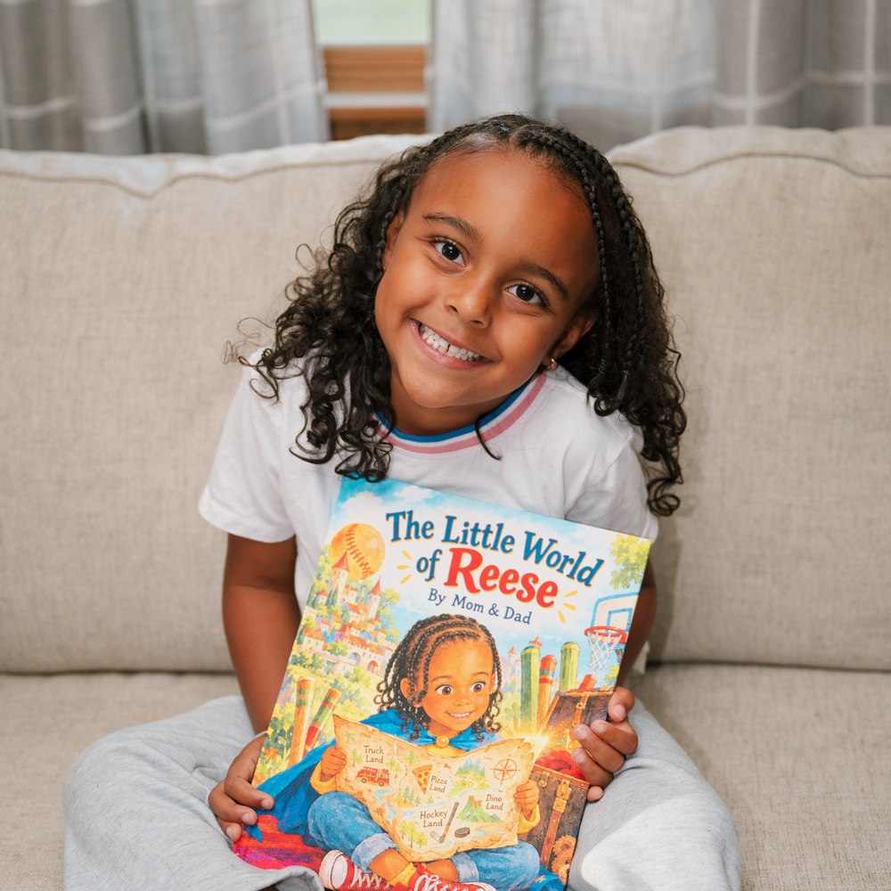 Reese smiling while holding The Little World of Reese, with her name and illustrated likeness on the printed cover