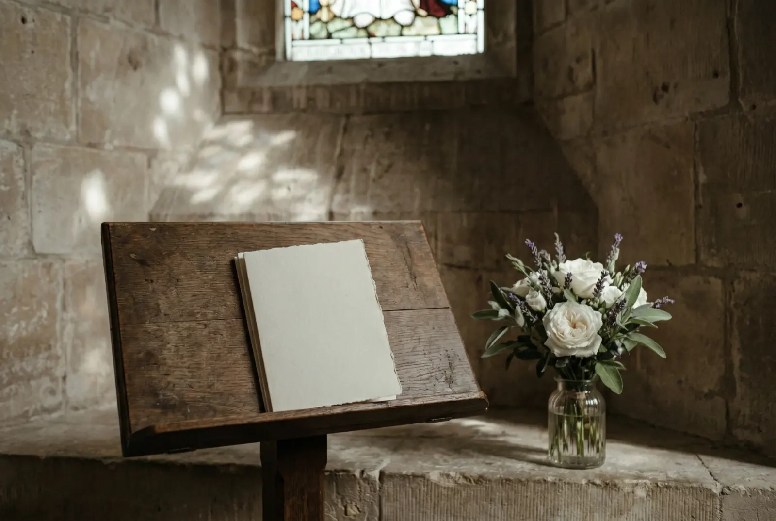 A wooden church lectern with a folded order of service, a posy of garden flowers in a small glass, soft natural light through clear windows — the moment before a eulogy is read.